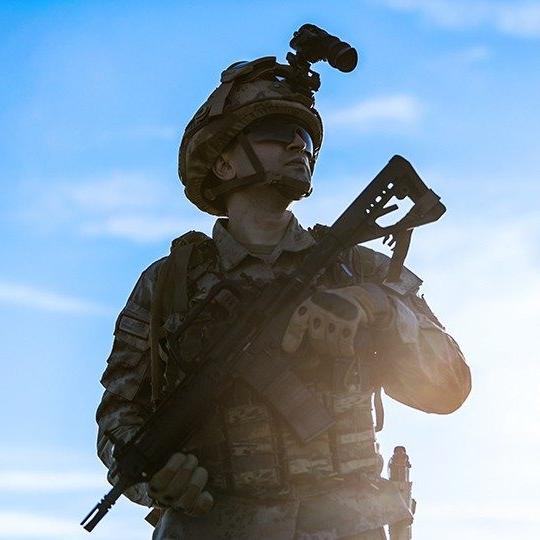 Military man dressed in a combat uniform, holding a weapon and looking up at the sky